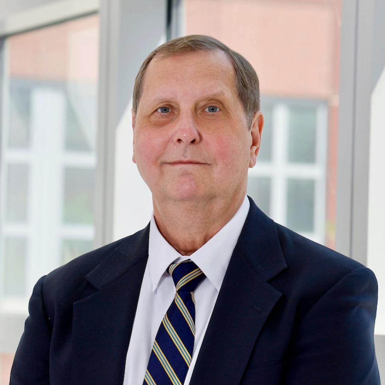 Caucasian man with dark blue jacket and tie with stripes