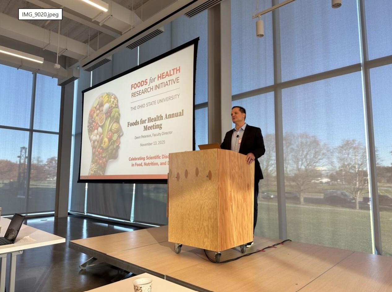 A speaker presenting in front of a slideshow featuring our welcome screen